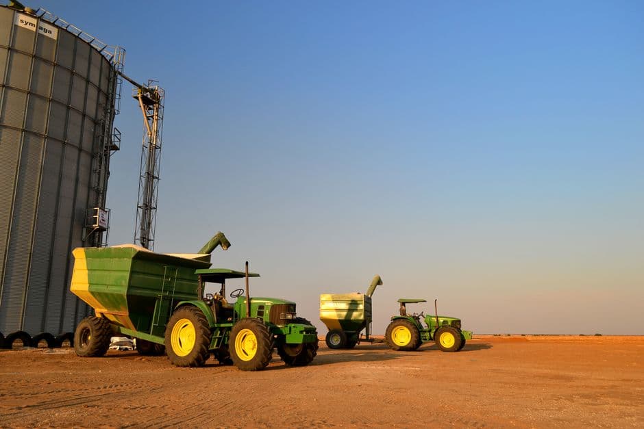 Tractors with grain carts parked beside a steel grain silo on a South African farm.